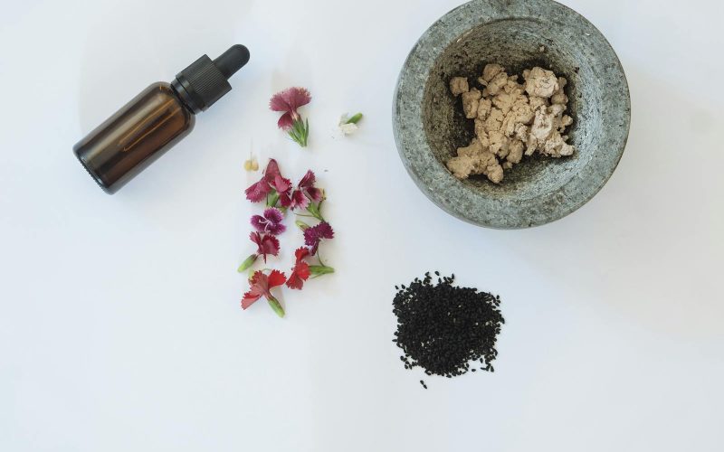 Flat lay of natural skincare ingredients including flowers, black seeds, and a dropper bottle.